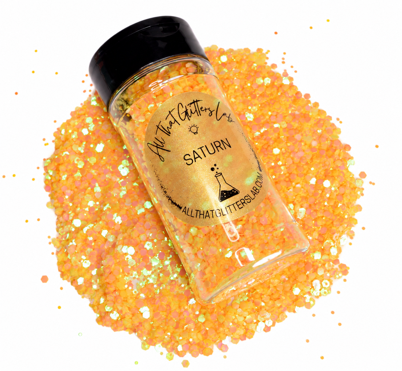 A clear plastic bottle of All That Glitters Lab 'Saturn' glitter, filled with shimmering orange, gold, and iridescent glitter, resting on top of a larger pile of the same glitter on a white background.