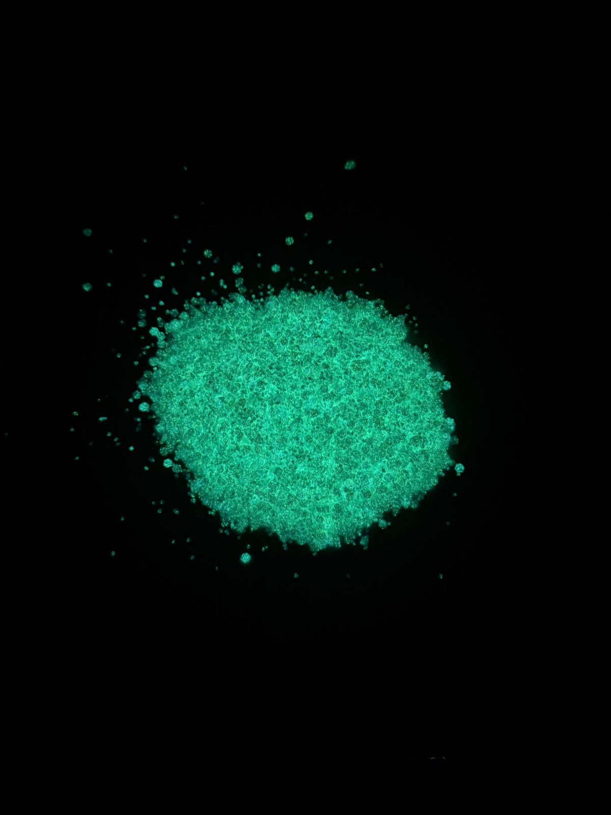 A small pile of bright fluorescent green glitter scattered on a solid black background.